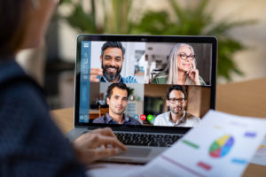 Back view of business woman talking to her colleagues about business plan in video conference. Multiethnic business team using laptop for a online meeting in video call. Group of businessmen and businesswomen smart working from home.